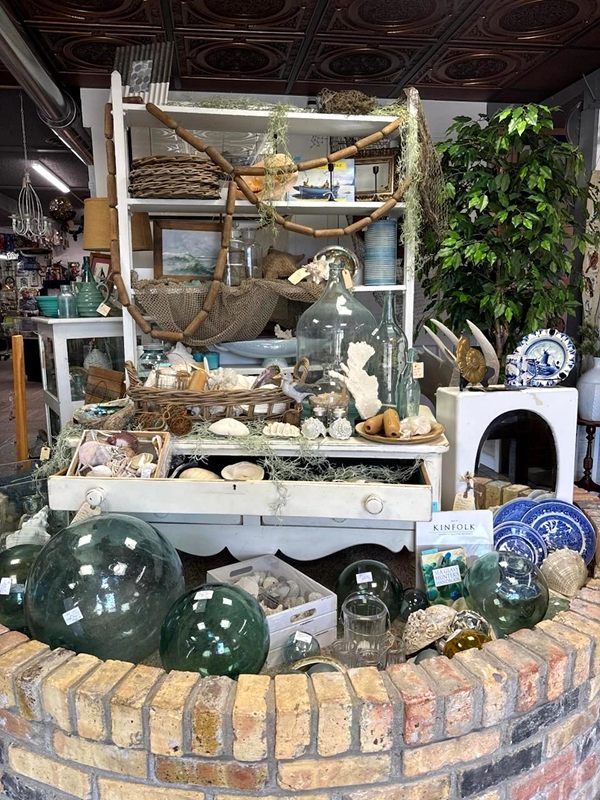 A seaside vignette of shells, glass fishing floats, a driftwood shelf and a blue-and-white plate