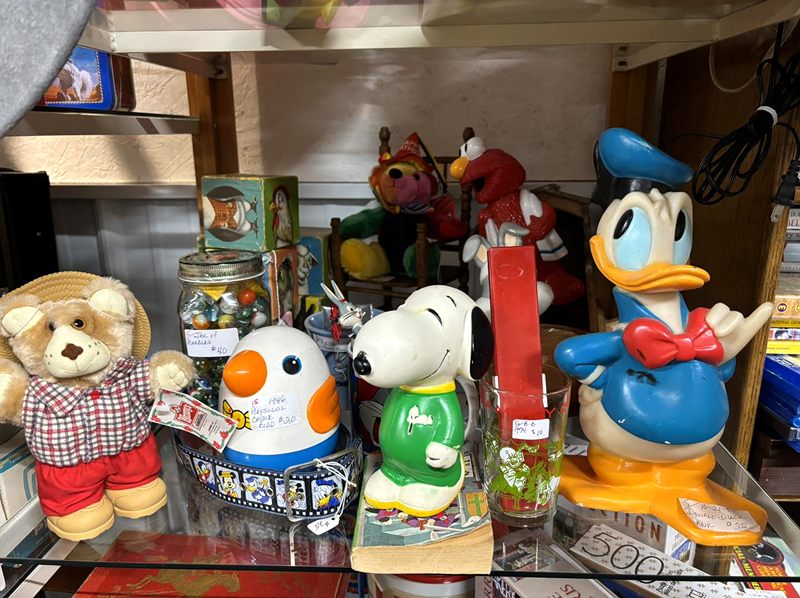 Cartoon character collectibles on a glass shelf, including Donald Duck, Snoopy and Elmo