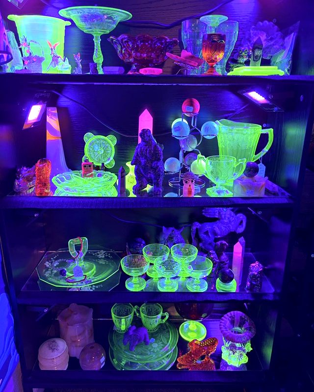 Green glassware glowing under a blacklight on a lit display shelf