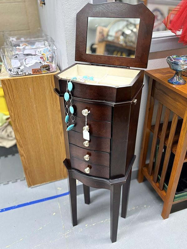 A dark wood jewelry armoire on tall legs with its mirrored lid open
