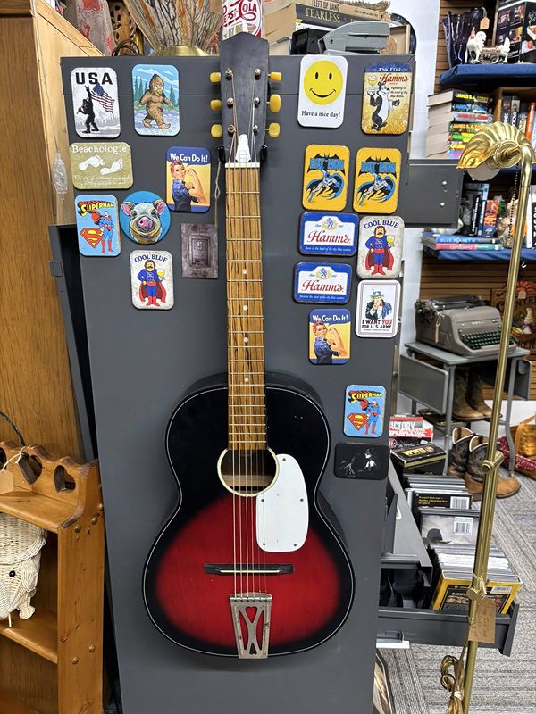 Superhero and retro magnets on a display next to a red acoustic guitar