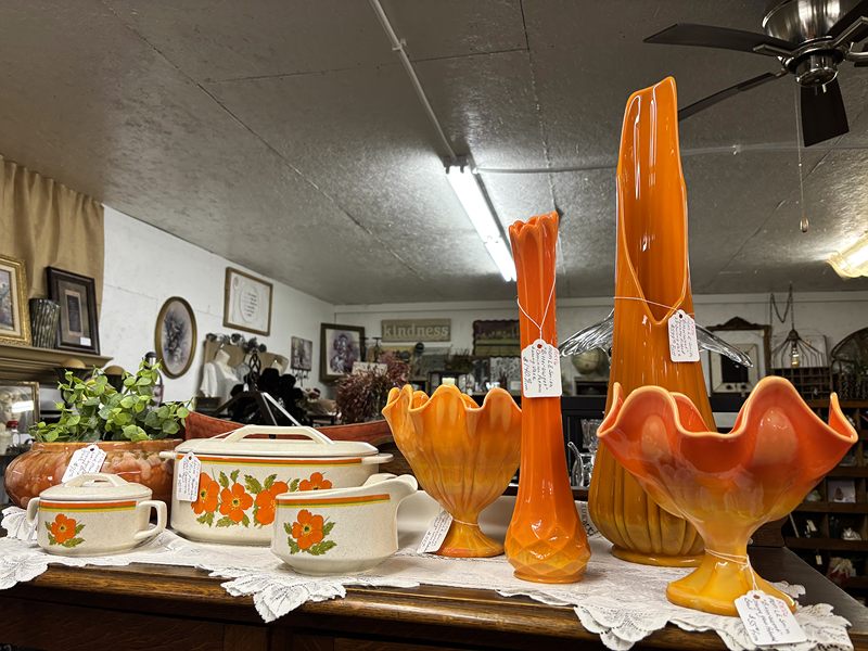 Orange glass vases and flowered casserole dishes on a lace-covered table
