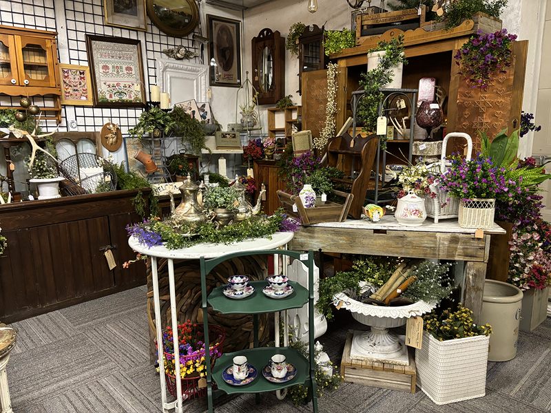 A garden-themed display with flowers, a green tiered stand of teacups and wooden hutches