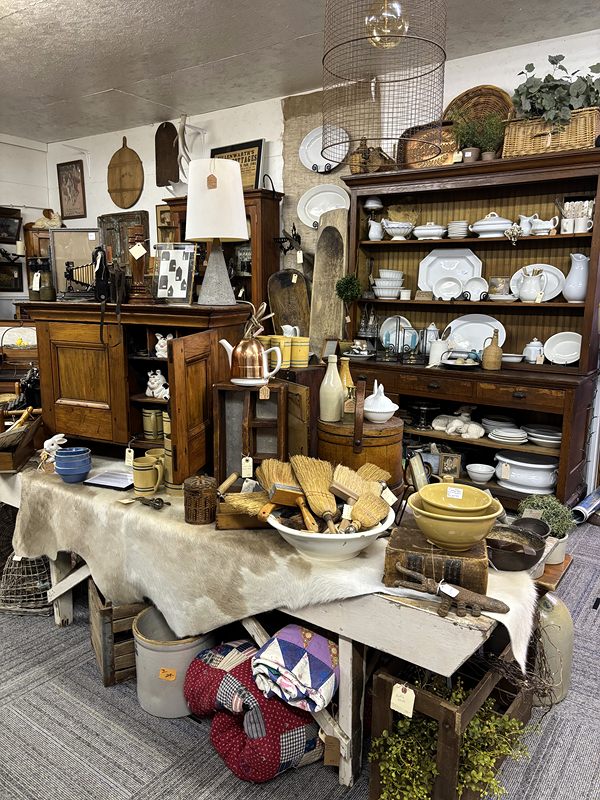 A hutch of white dishes and a table of wooden bowls, crocks and patchwork pillows