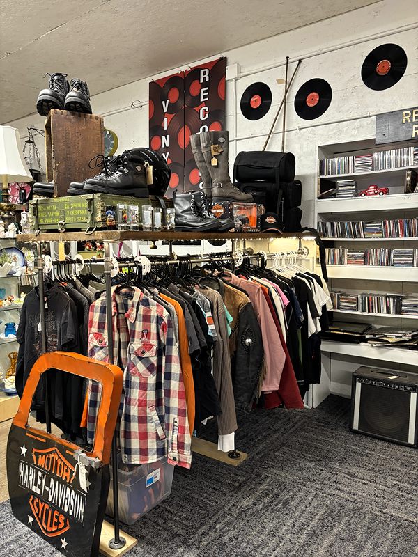 Racks of shirts and jackets with boots on a top shelf and vinyl records on the wall