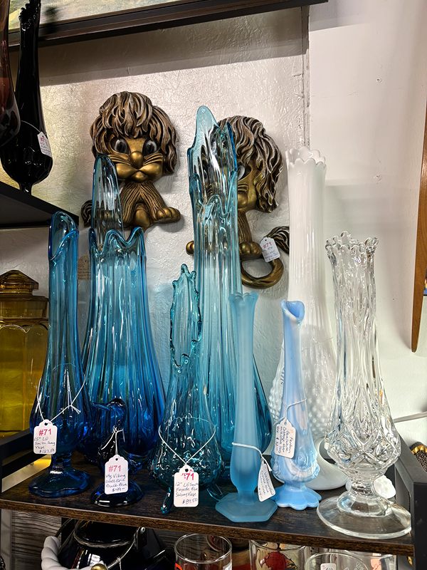 Tall blue, clear and frosted glass vases beside two lion-head wall plaques