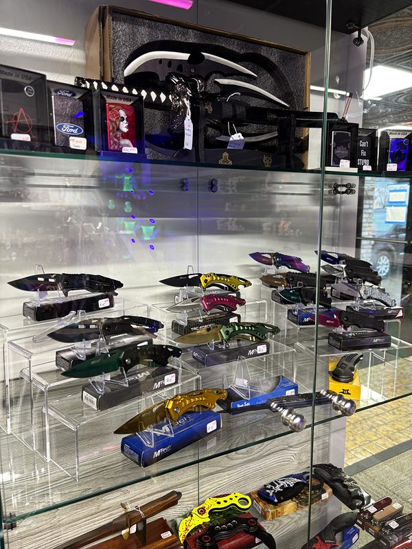 A glass display case of folding knives with colorful handles