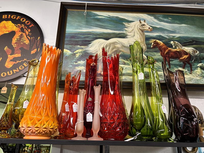 Tall orange, red and green glass vases in front of a painting of horses