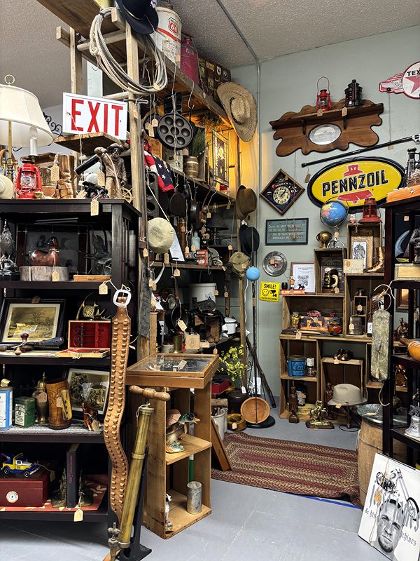 A rustic corner with lanterns, tools, a Pennzoil sign and an old exit sign