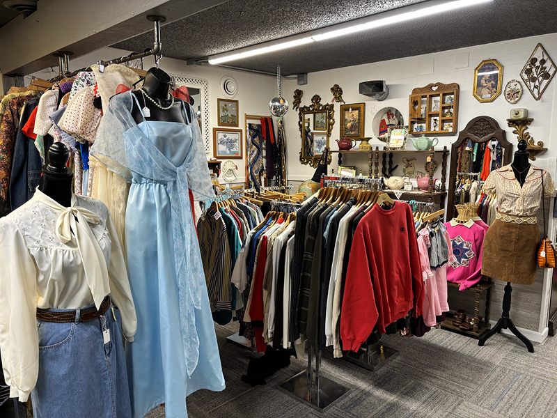 Vintage dresses and blouses on mannequins in front of racks of clothing