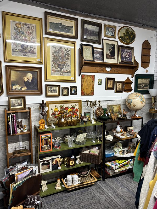 A wall of framed pictures above shelves of glassware and figurines