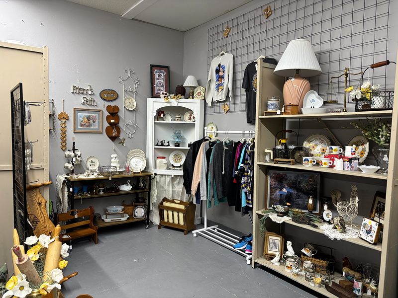 A corner with a shelf of dishes, a table lamp and a small clothing rack