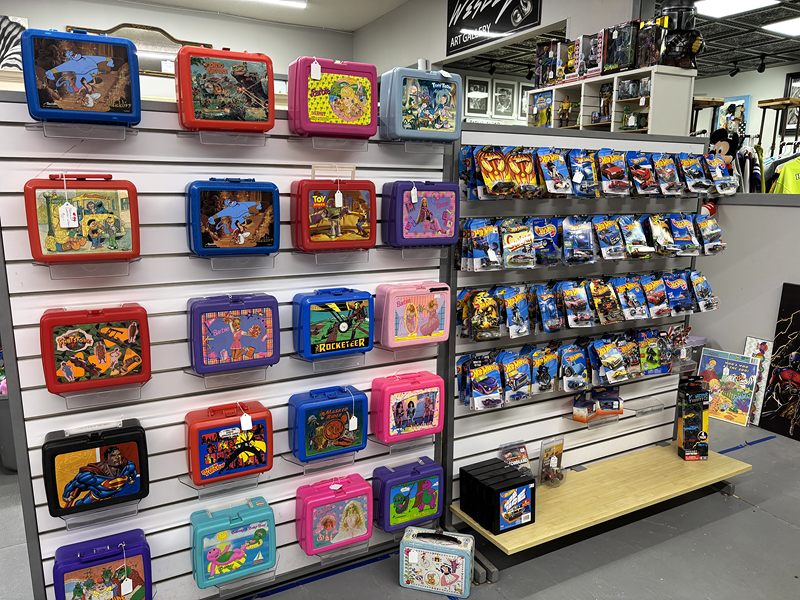A wall of vintage metal lunch boxes beside racks of packaged toy cars
