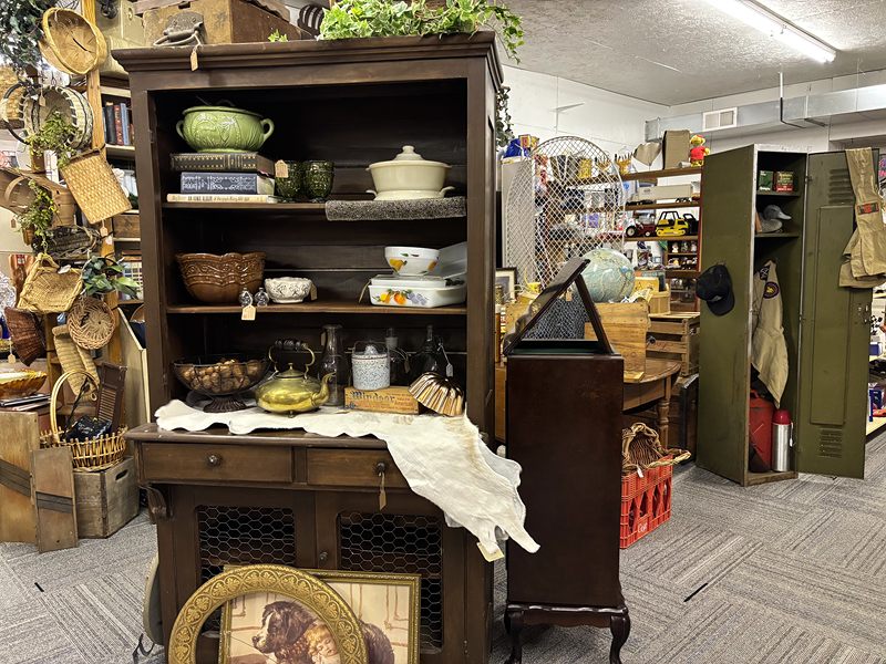 A dark wood hutch with bowls and a brass kettle, surrounded by baskets