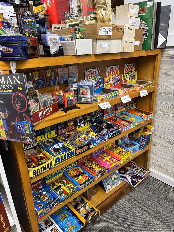 A wooden rack of boxed trading cards and vintage toys, including Batman