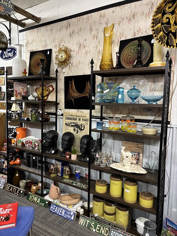 Metal shelves of yellow canisters, blue glass and mannequin heads above old street signs