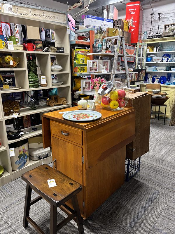 A wooden desk and stool in front of shelves of kitchenware and décor