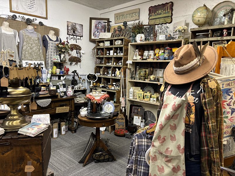 A home décor room with a hat and apron on a mannequin and shelves of décor behind